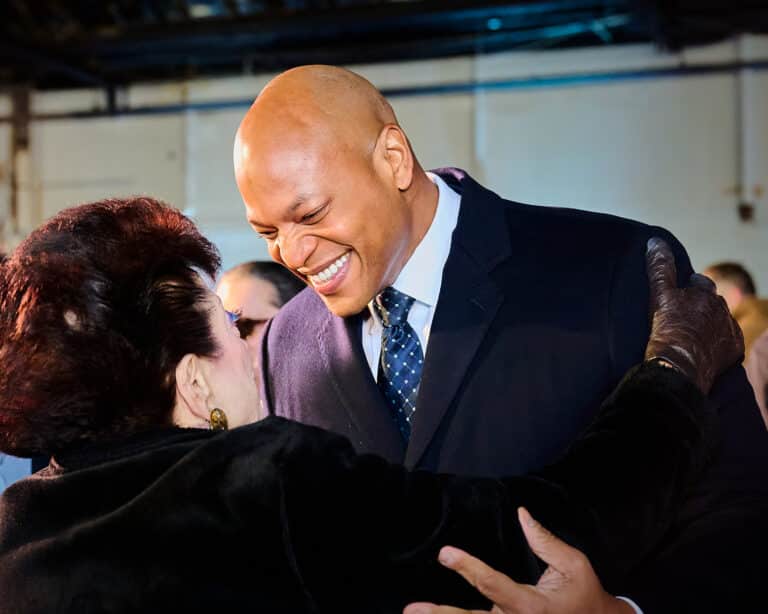 Professional event photograph of Maryland Governor Wes Moore at the Pikesville Armory Foundation Groundbreaking event where we was the featured speaker, wearing a dark blue suit, tie, and white dress shirt, and is greeting an event guest, taken by corporate event photographer Heidi Marie Bell in Pikesville, Maryland.